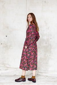 Sustainable cotton floral dress. Bloomsbury style. Drawstring waist. Long sleeve.  Round, notched neck.  Hot pinks and greens on a black ground. Made in England 