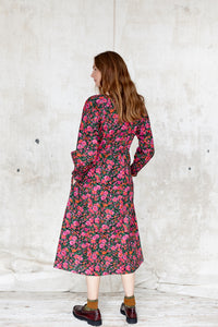 Sustainable cotton floral dress. Bloomsbury style. Drawstring waist. Long sleeve.  Round, notched neck.  Hot pinks and greens on a black ground. Made in England 