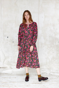 Sustainable cotton floral dress. Bloomsbury style. Drawstring waist. Long sleeve.  Round, notched neck.  Hot pinks and greens on a black ground. Made in England 