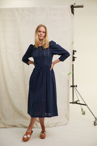 Navy cotton broderie dress. Gathered skirt. Side slip pockets. Back zip. Lined with cream cotton. Mid calf length. Easy fit. Long sleeve. 100% cotton