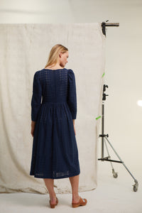 Navy cotton broderie dress. Gathered skirt. Side slip pockets. Back zip. Lined with cream cotton. Mid calf length. Easy fit. Long sleeve. 100% cotton
